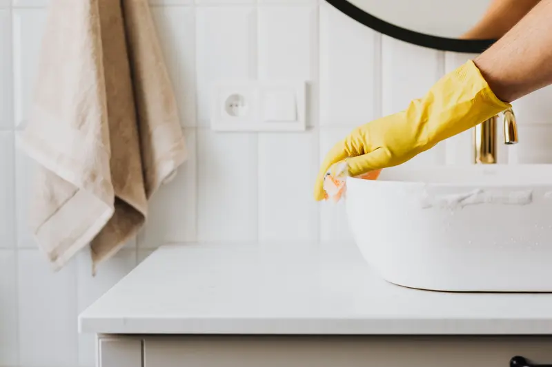 Gloved hand wiping the rim of a white bathroom basin