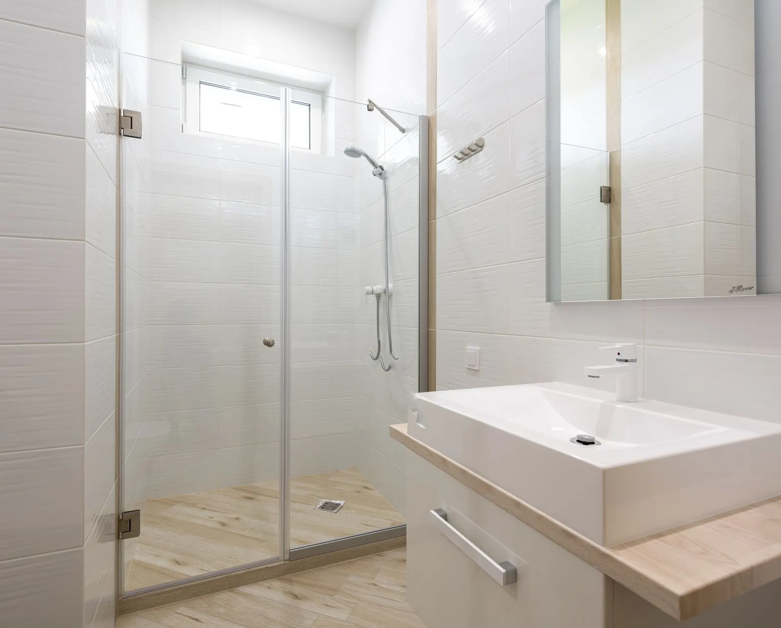 A bathroom with a glass shower, a white sink and a mirror
