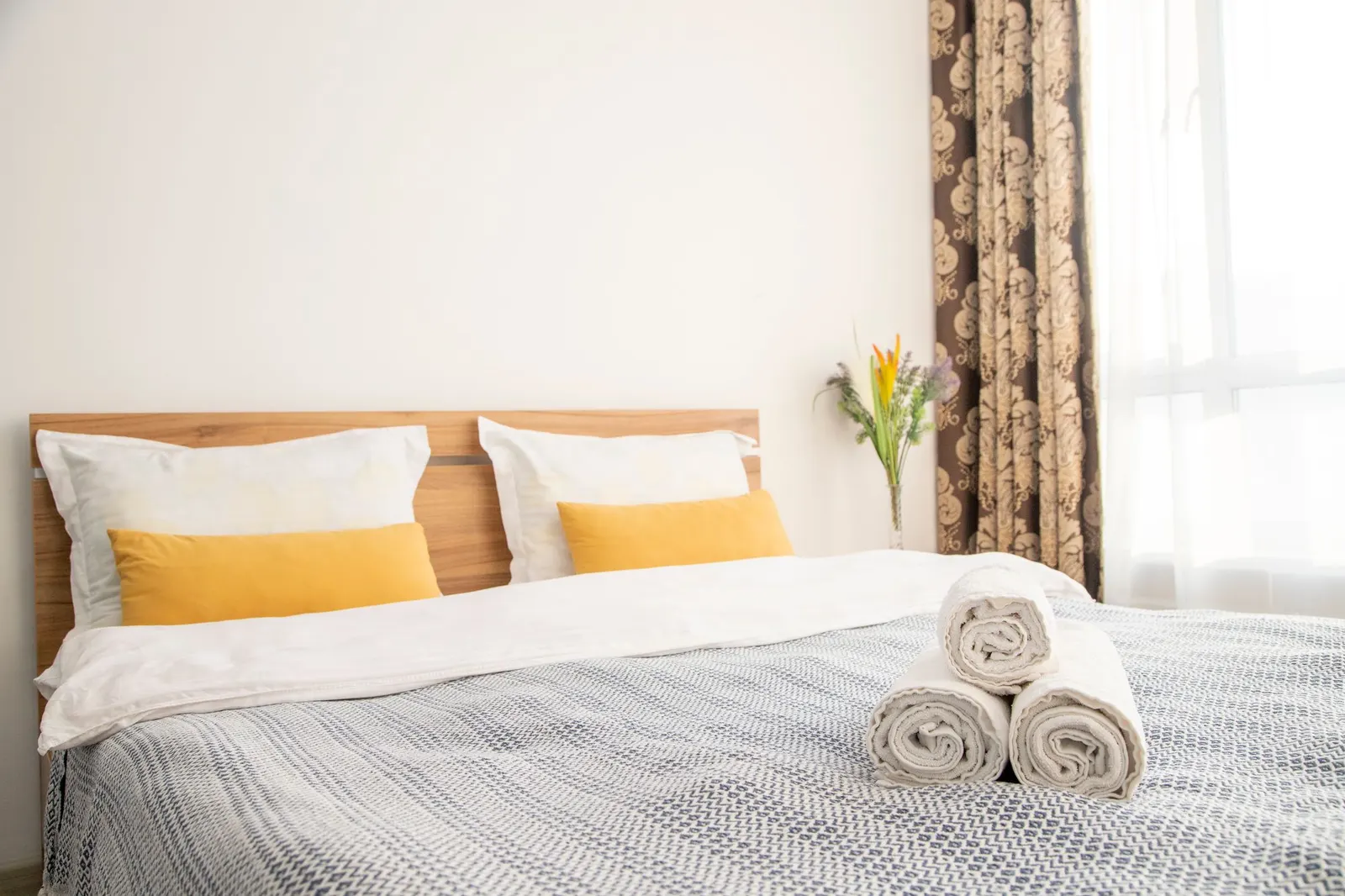 Made bed with yellow pillows and rolled towels in a bright bedroom