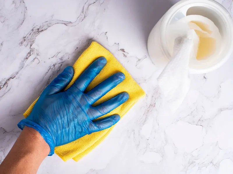 Gloved hand wiping a marble countertop with a yellow cloth