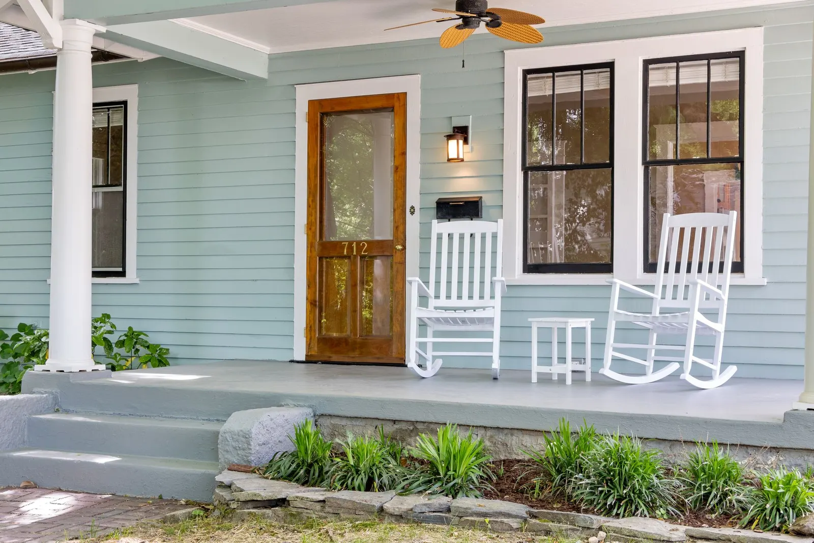 A front porch with white rocking chairs and a wooden front door